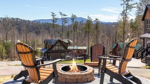 Eine Holzhütte mit Feuerstelle und zwei Adirondack-Stühlen vor einer Bergkulisse.