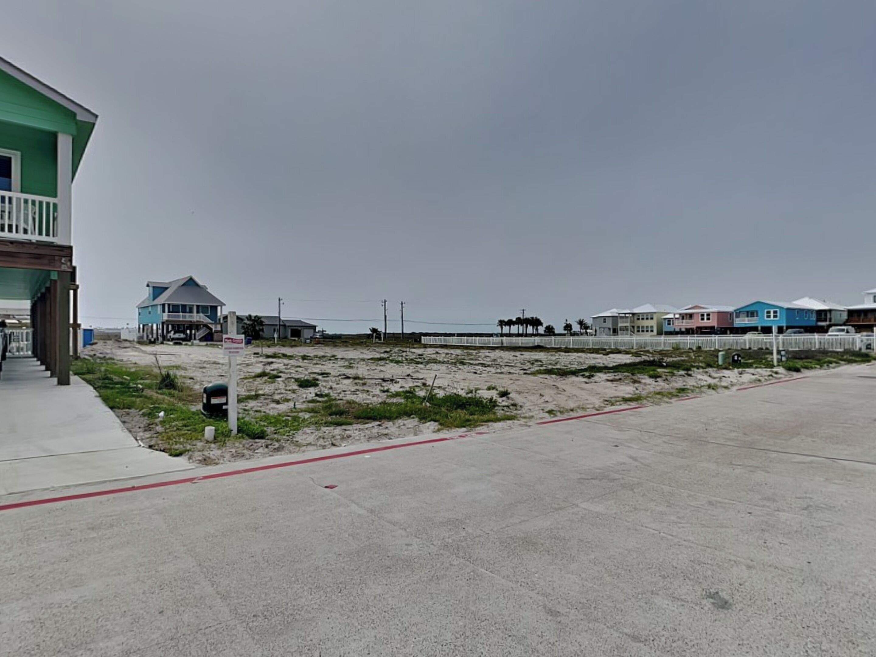 A coastal property with a sandy beach, a wooden pier, and colorful houses in the background.