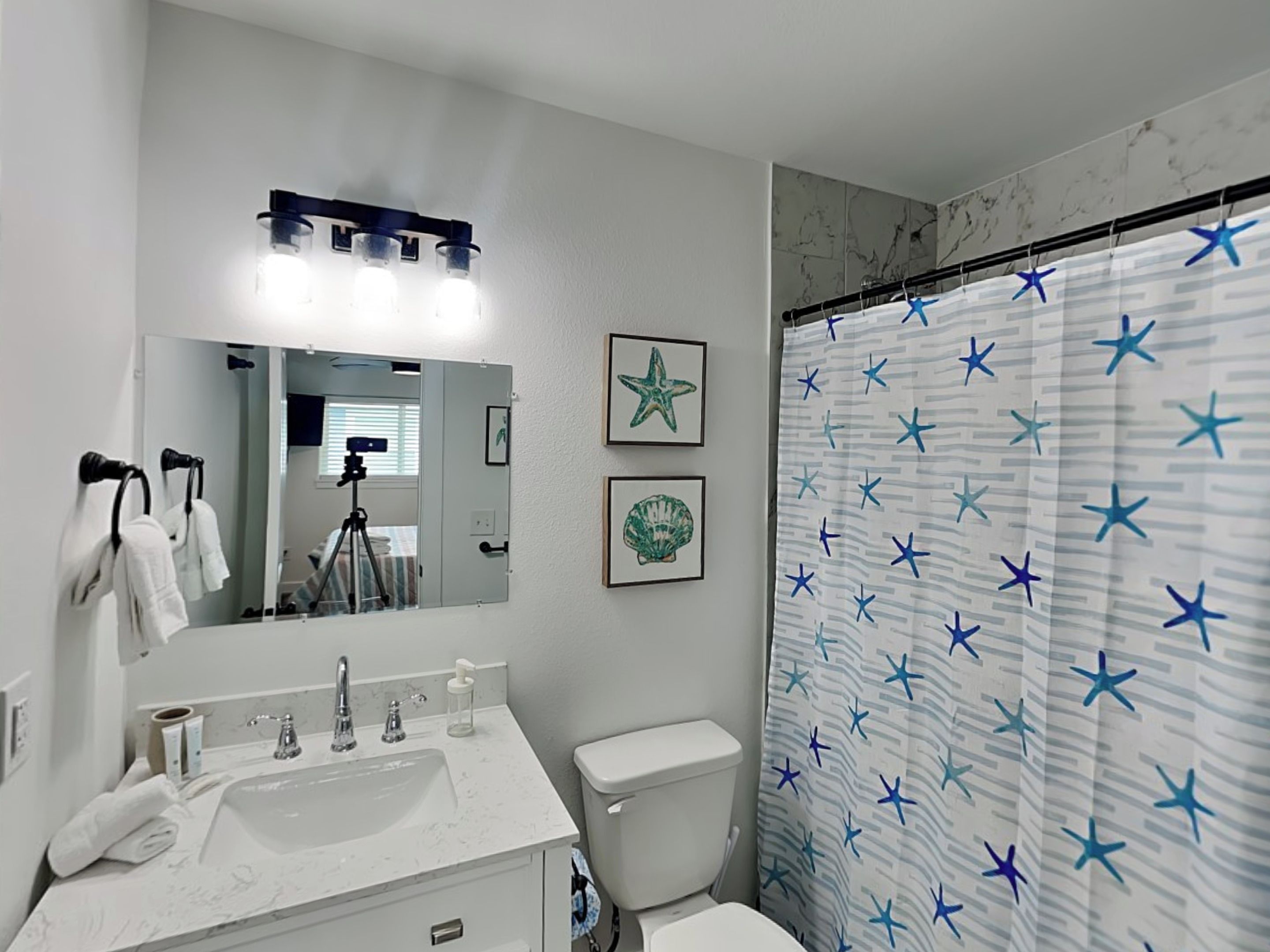A bathroom with a white sink, mirror, and toilet. There is a shower curtain with a star pattern.