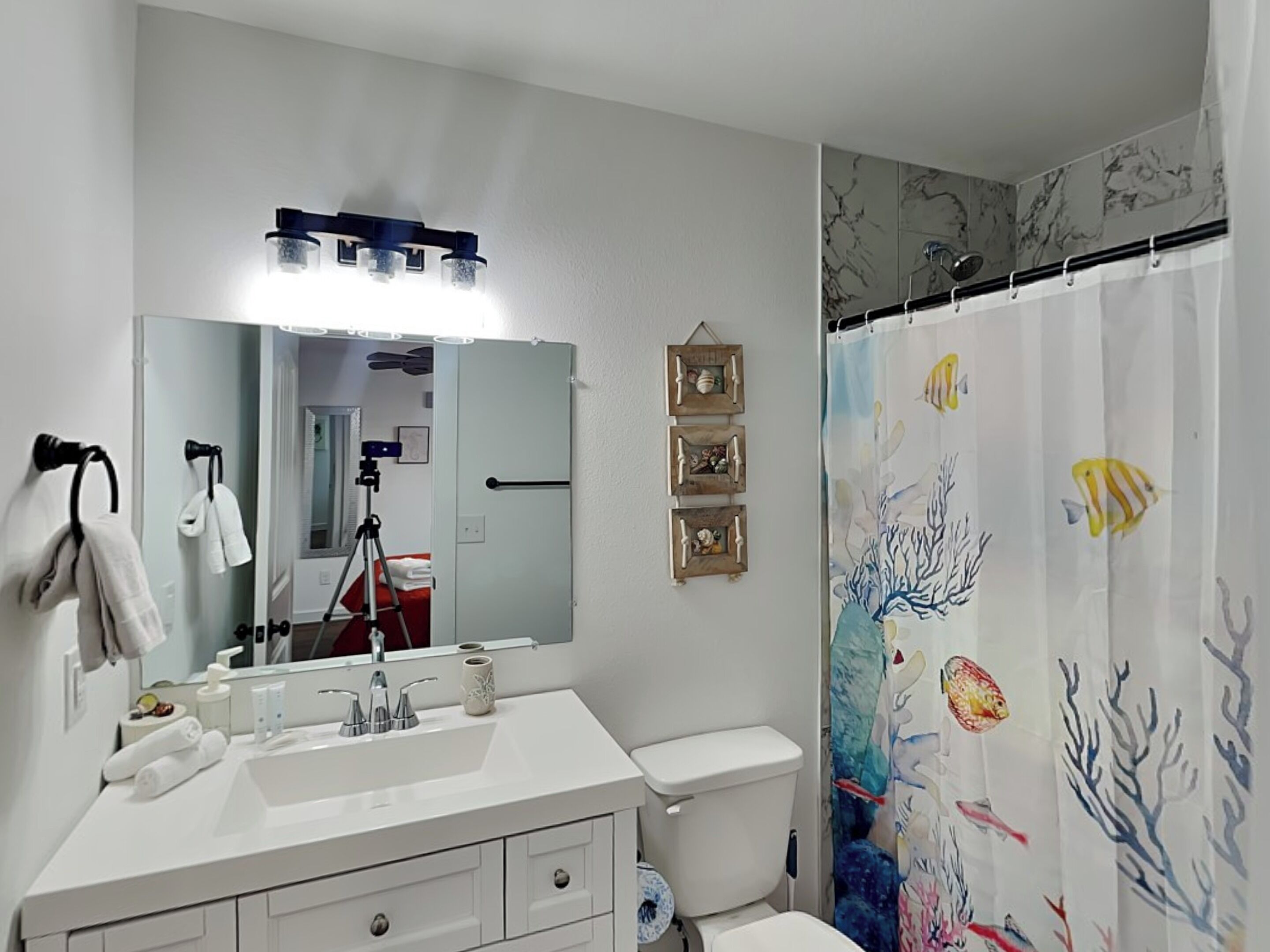 Ein Badezimmer mit einem weißen Waschbecken, Spiegel und WC. Ein Duschvorhang mit einem Meereslebewesen-Motiv.