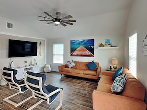 A living room with a TV, two sofas, a ceiling fan, and a wooden floor.