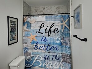 A bathroom with a shower curtain featuring a beach theme, including starfish and waves.