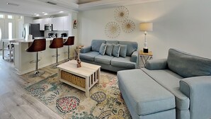 A modern living room with a sofa, a coffee table, and a dining area with chairs. - Palm Coast Hideaway by Distinctive Beach Rentals (Palm Coast)