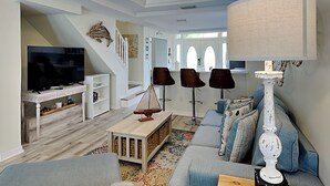 A modern living room with a TV, sofa, and lamps. - Palm Coast Hideaway by Distinctive Beach Rentals (Palm Coast)