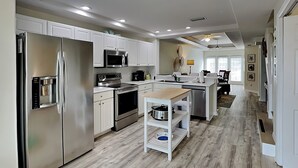 A modern kitchen with stainless steel appliances, white cabinetry, and a central island with a sink and storage. - Palm Coast Hideaway by Distinctive Beach Rentals (Palm Coast)