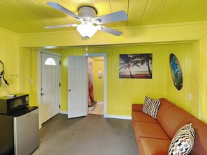 A room with a ceiling fan, a microwave, a couch with patterned pillows, and a door leading to another room. - Seagull's Landing by Ryson Vacation Rentals (Galveston)