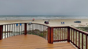 Een houten terras met een leuning, uitkijkend op een strand.