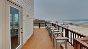 A wooden deck with outdoor seating, a glass door, and a view of the beach and ocean. - Seaside Eden by Ryson Vacation Rentals (Freeport)