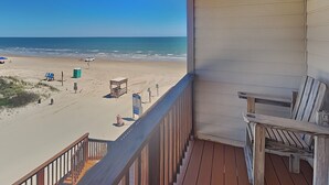 Een balkon met uitzicht op het strand, een houten terras en een stoel.