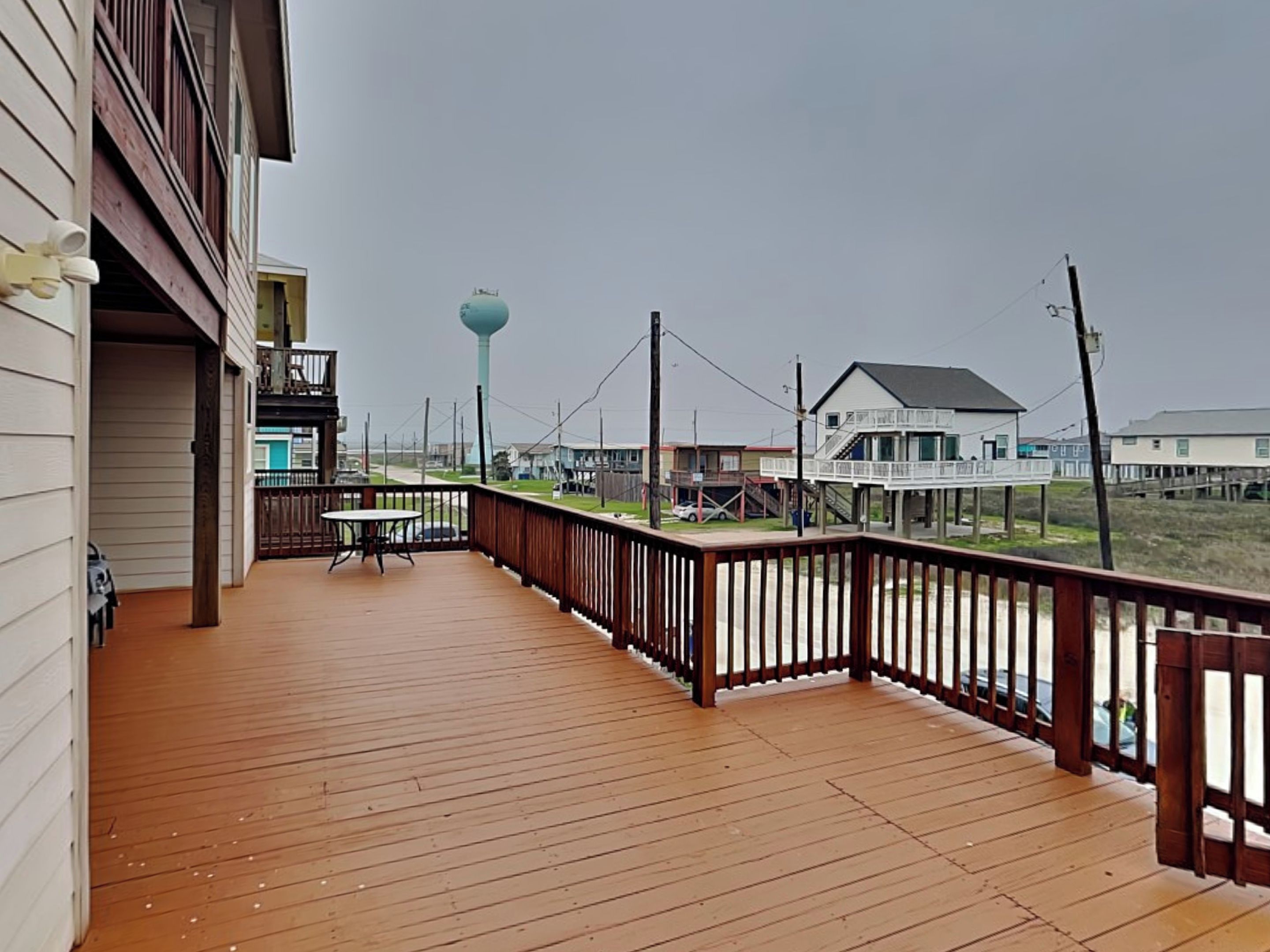 Eine Holzterrasse mit Geländer, die auf einen Strand mit Häusern und einem Wasserturm blickt.