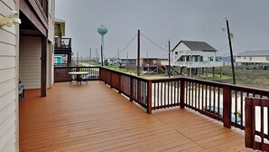 A wooden deck with a railing, overlooking a beach area with houses and a water tower. - Seaside Eden by Ryson Vacation Rentals (Freeport)