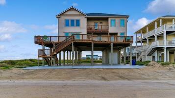 A two-story beachfront house with a wooden deck and a balcony.