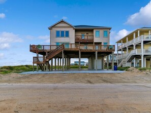 A two-story beachfront house with a wooden deck and a balcony.