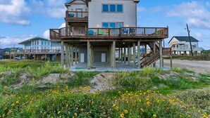 A two-story beachfront house with a balcony, a covered porch, and a staircase leading to the upper level.