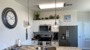 Una cocina moderna con una isla central, armarios blancos, electrodomésticos de acero inoxidable e iluminación colgante.