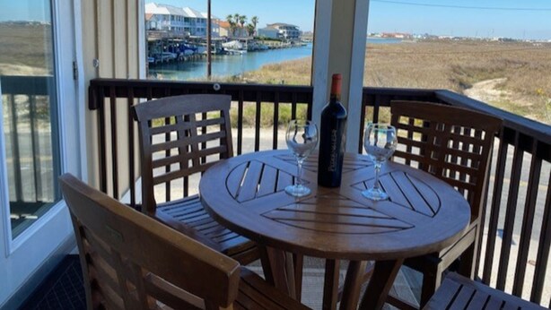 Una mesa de madera con dos sillas en un balcón con vistas a un puerto deportivo con barcos y una playa.