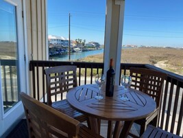 Una mesa de madera con dos sillas en un balcón con vistas a un puerto deportivo con barcos y una playa.