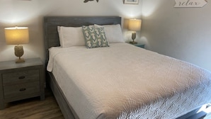 Una cama bien tendida con colcha blanca, dos mesitas de noche con lámparas y decoración en la pared con motivos de estrellas de mar y tortugas.