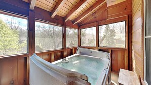 A wooden cabin with a hot tub, large windows, and a view of trees. - Smokey Bear Haven by Jackson Mountain Rentals (Pigeon Forge)