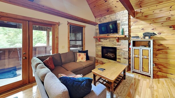 A cozy living room with a stone fireplace, wooden ceiling beams, and a television mounted above it. - Smokey Bear Haven by Jackson Mountain Rentals (Pigeon Forge)