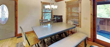 A dining area with a wooden table, chairs, a bench, and a chandelier.