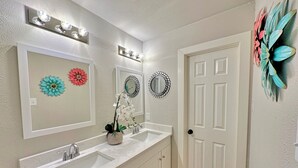 Un baño con tocador blanco, lavamanos, espejo y decoración mural.