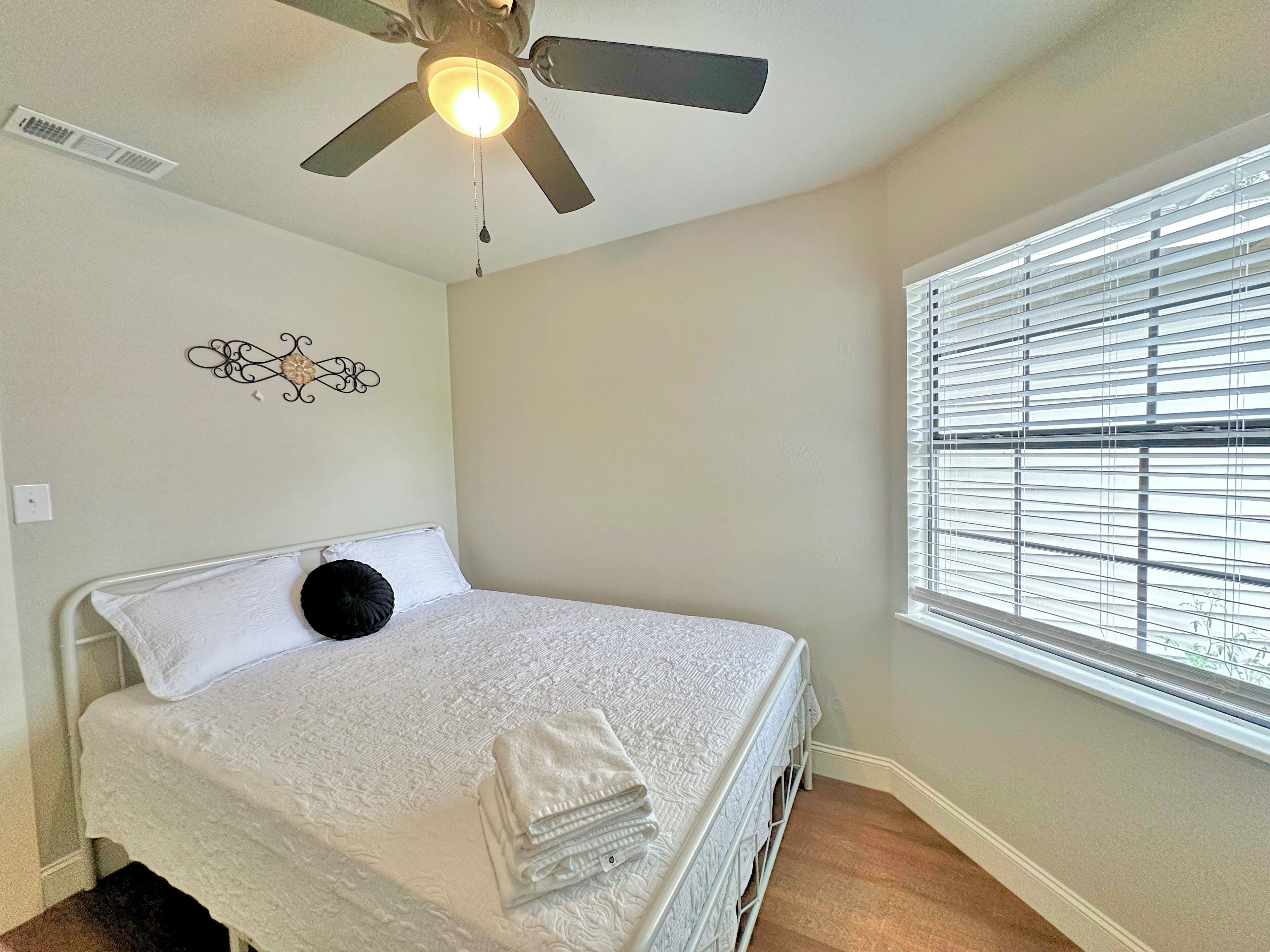 A bedroom with a bed, a ceiling fan, a window with blinds, and a wall decoration.