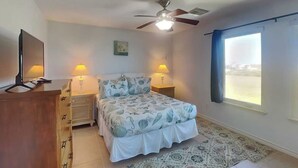 Un dormitorio con cama, dos lámparas de noche, ventilador de techo, televisión y ventana con vistas.