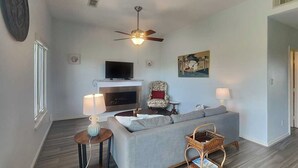 Una sala de estar con un sofá, un televisor, una chimenea, un ventilador de techo y un cuadro en la pared.