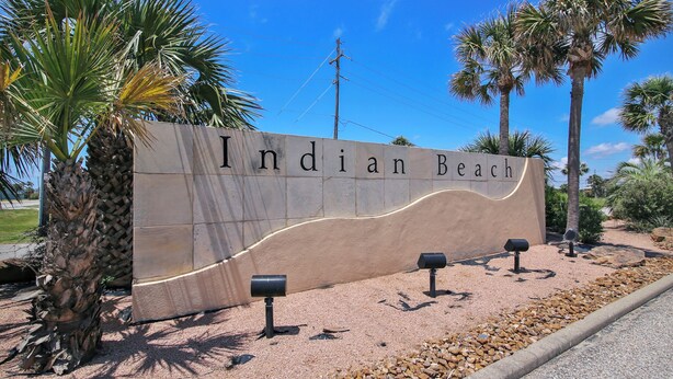 Señal de Indian Beach con un diseño curvo, palmeras y un cielo despejado.