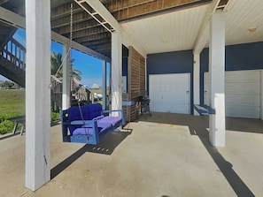 A covered outdoor area with a swing seat, a garage door, and a concrete floor. - Splish Splash Oasis by Ryson Vacation Rentals (Galveston)