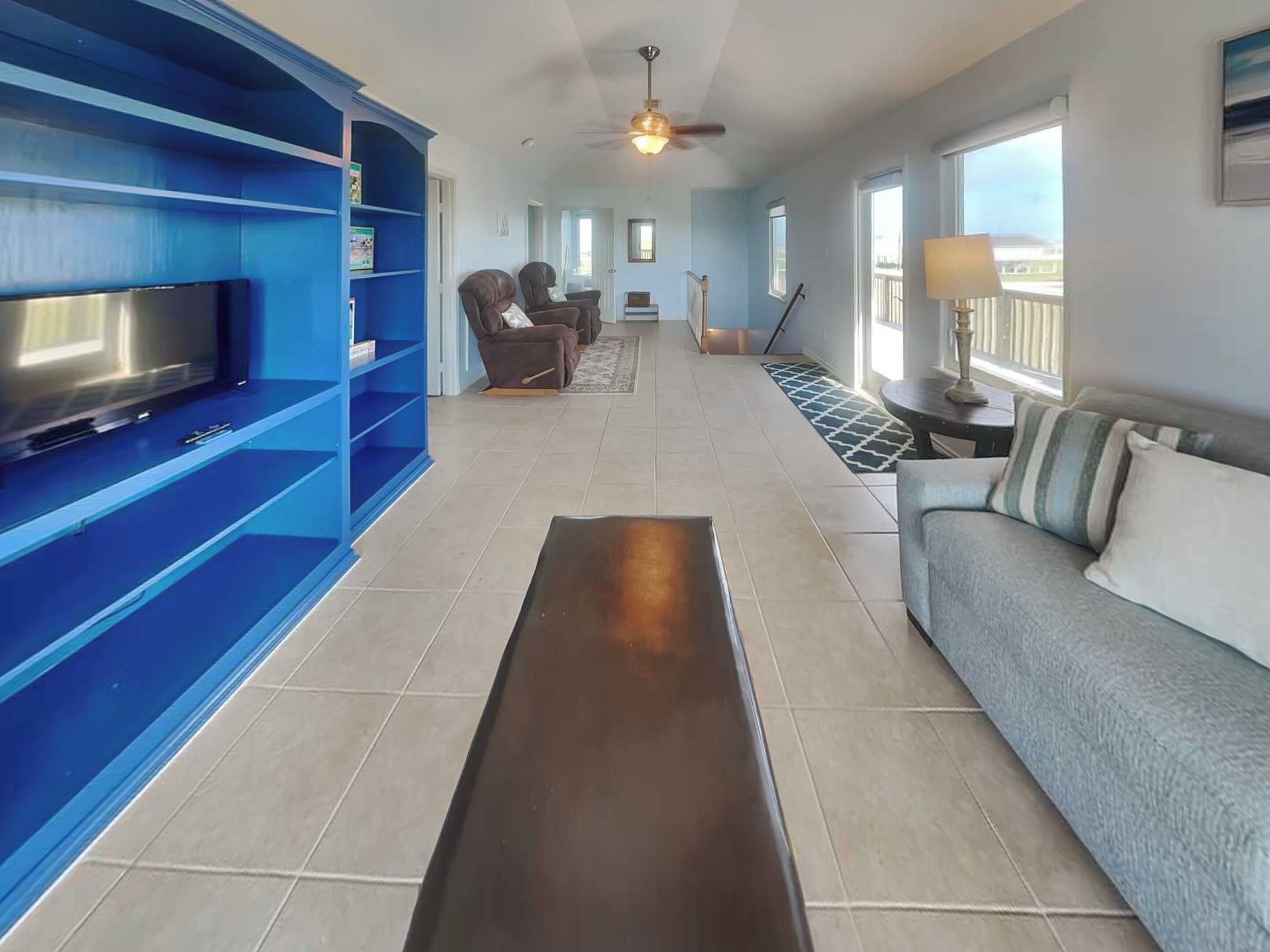 A living room with a flat-screen TV, blue shelving, a grey sofa, and a ceiling fan.