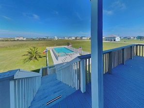 A pool with a wooden deck and railing, surrounded by a grassy area and houses in the background. - Splish Splash Oasis by Ryson Vacation Rentals (Galveston)