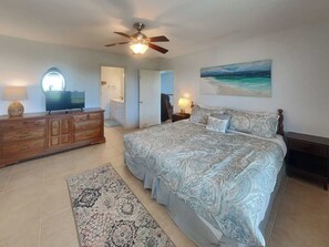 A bedroom with a bed, dresser, ceiling fan, and a painting of a beach. - Splish Splash Oasis by Ryson Vacation Rentals (Galveston)