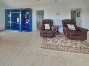 A living room with two brown armchairs, a patterned rug, and a blue bookshelf. - Splish Splash Oasis by Ryson Vacation Rentals (Galveston)