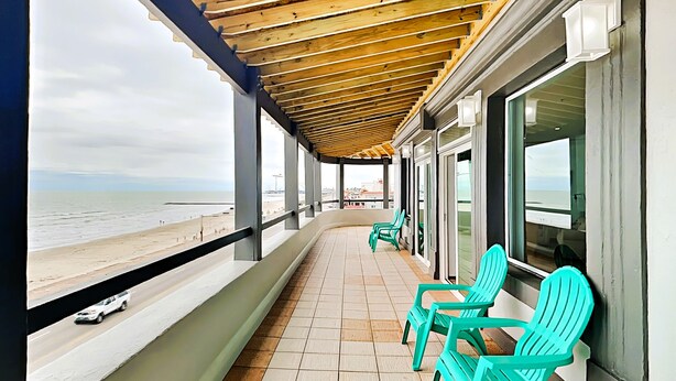 A balcony with turquoise chairs, a tiled floor, and a view of the beach. - Sunset On The Seawall #1 by Ryson Vacation Rentals (Galveston)