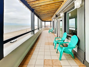 A balcony with turquoise chairs, a tiled floor, and a view of the beach. - Sunset On The Seawall #1 by Ryson Vacation Rentals (Galveston)