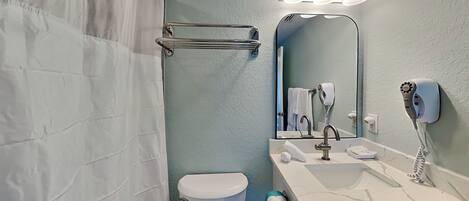 Een badkamer met douchegordijn, toilet, wastafel met spiegel en een aan de muur bevestigde haardroger.