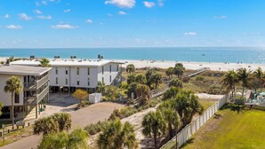 Une propriété située en bord de mer, avec un bâtiment blanc, une plage de sable et un ciel bleu dégagé.