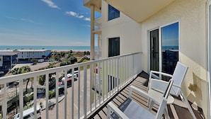 Un balcon avec vue sur la plage, un espace de stationnement et un bâtiment en arrière-plan.