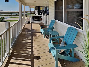 A wooden deck with blue Adirondack chairs, a covered area with a railing, and a view of the water. - The Driftwood by Silver Sands Vacation Rentals (Port Aransas)