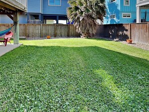 A backyard with a wooden fence, a palm tree, and a hammock. - The Driftwood by Silver Sands Vacation Rentals (Port Aransas)
