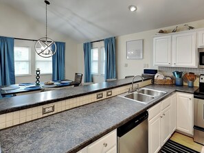 A modern kitchen with white cabinets, a granite countertop, a dishwasher, and a sink. - The Driftwood by Silver Sands Vacation Rentals (Port Aransas)