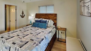 Ein Schlafzimmer mit hölzernem Kopfteil, einer gesteppten Bettdecke, einem Nachttisch mit Lampe, einem Deckenventilator und einem Fenster mit Jalousien.