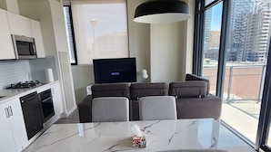 A modern kitchen with a dining area, large windows, and a flat-screen TV.