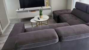 A modern living room with a sectional sofa, a flat-screen TV, a small round coffee table, and a decorative clock on the wall.