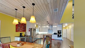 A modern kitchen with white cabinets, stainless steel appliances, and a wooden dining table with colorful chairs. - The Reel Mccoy by Miss Kitty’s (Rockport)