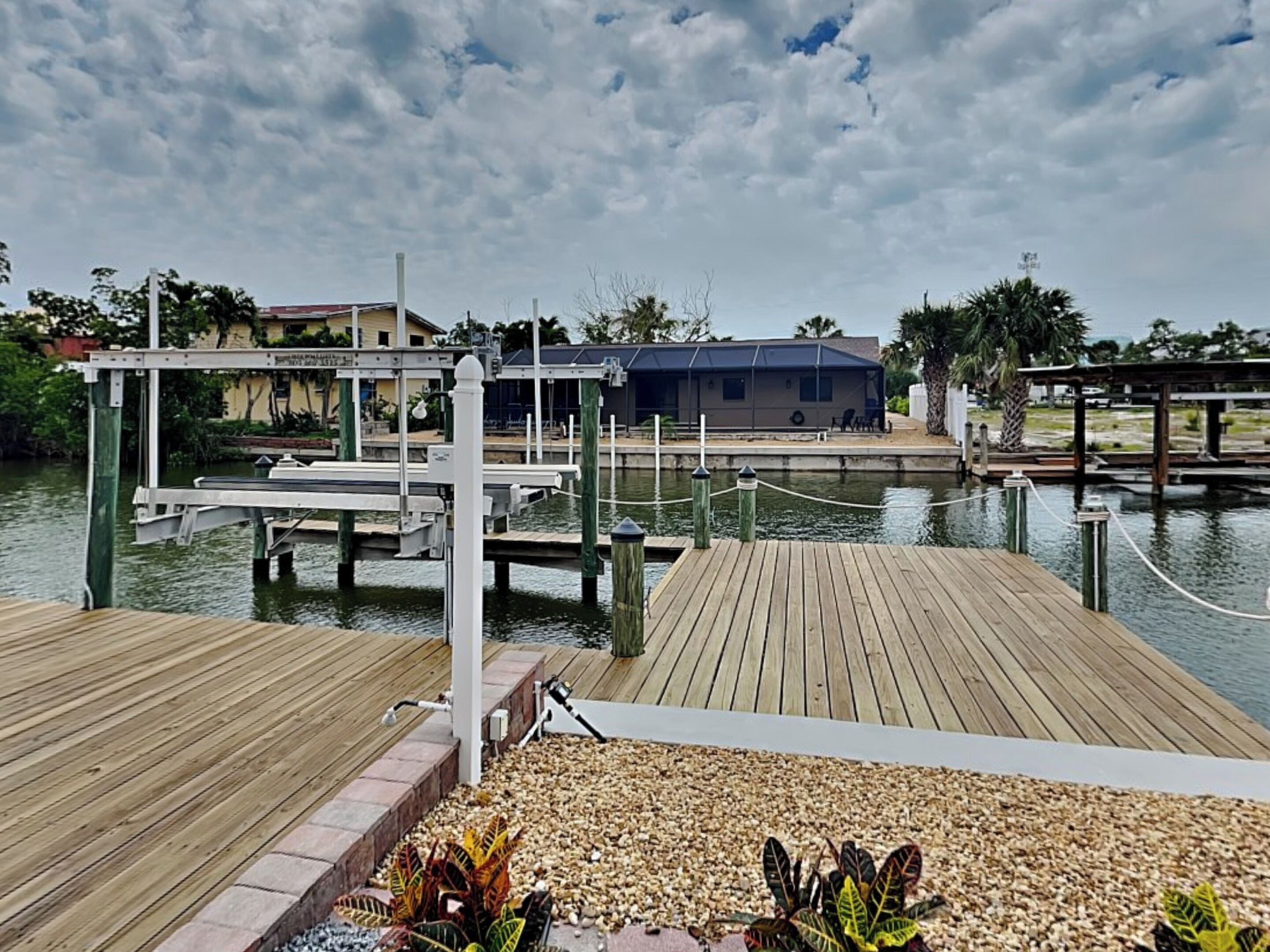 A waterfront dock area with wooden walkways, a boat house, and a small building in the background.