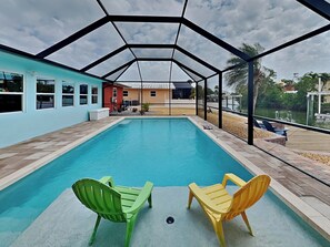 A covered outdoor swimming pool with two chairs, a view of buildings, and a clear sky.