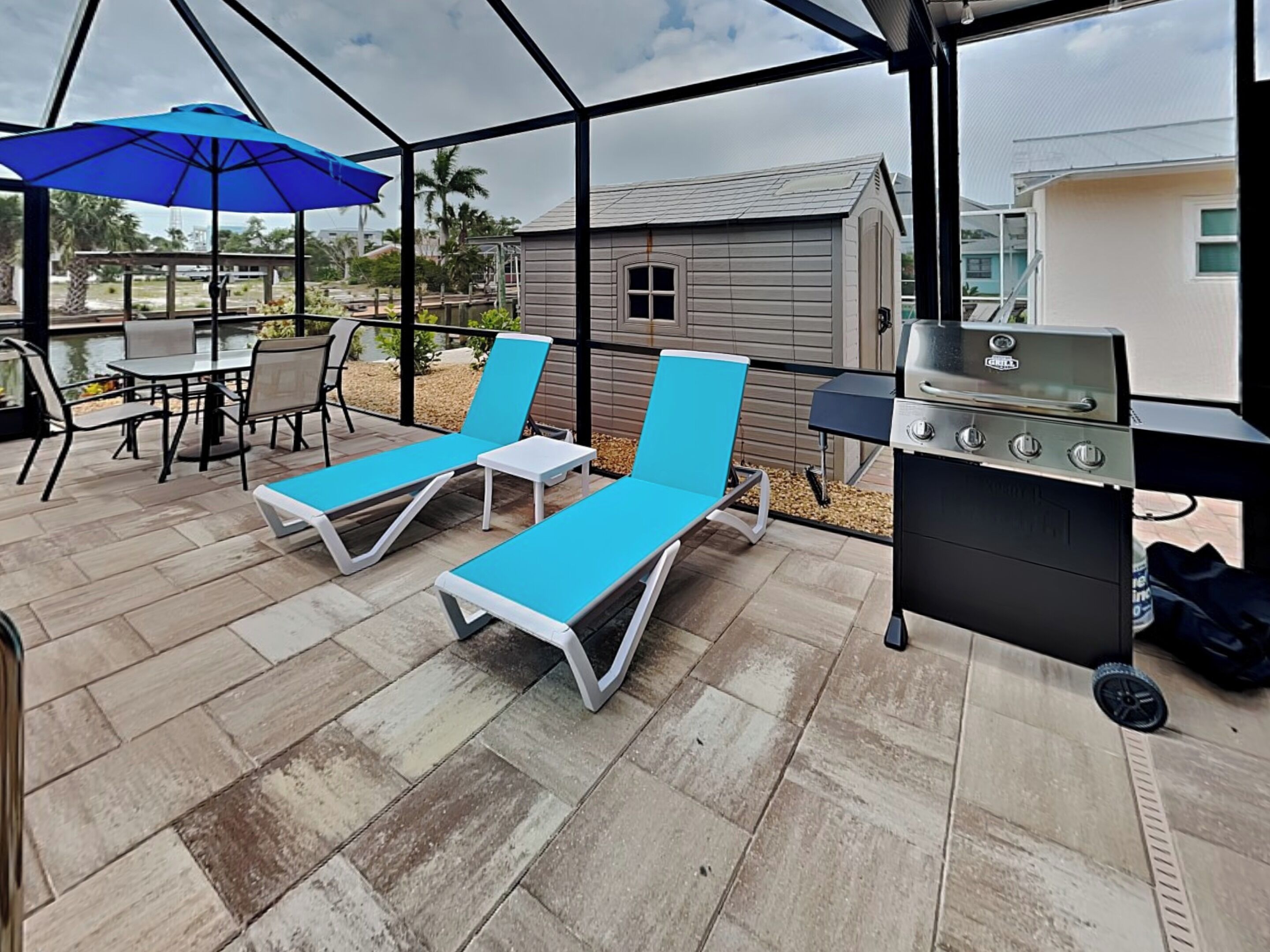 A covered patio with blue lounge chairs, a grill, and a table with chairs.